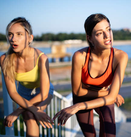 Beautiful women in sportswear drinking water, talking and resting after training outdoorsの写真素材