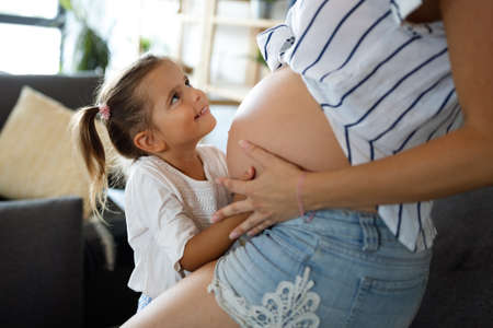 Happy kid girl hugging pregnant mothers bellyの写真素材