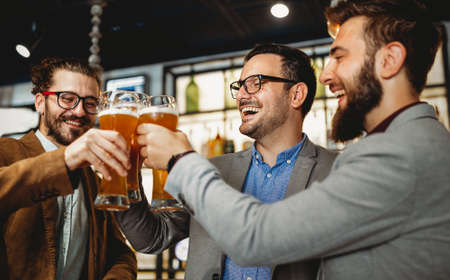 Leisure, friendship pub concept. Happy male friends drinking beer and clinking glasses at bar or pubの写真素材