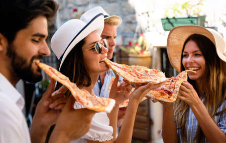 Happy group of people eating pizza outdoors,they are enjoying together.