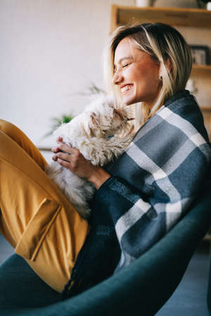 Beautiful woman playing with puppy on sofa at home