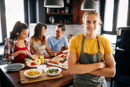 Group of happy friends laughing and talking while preparing meals in kitchenの写真素材