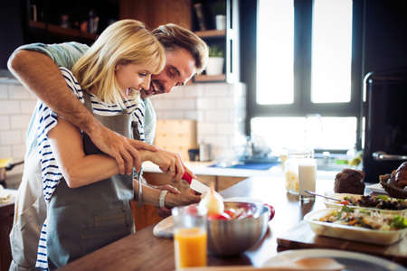 Beautiful young couple is talking and smiling while cooking healthy food in kitchen at homeの写真素材