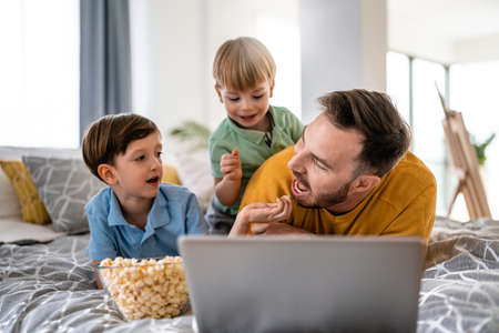 Handsome man and their children are using a laptop together on the bed at home