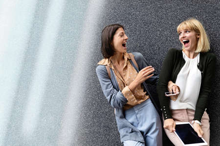 Two happy women are having fun together in the city. Technology, people fun conceptの写真素材