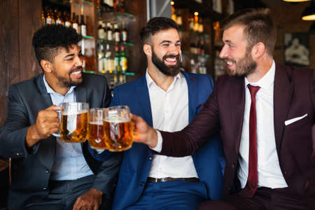 Happy young businessmen drinking beer and talking at pub after workの写真素材