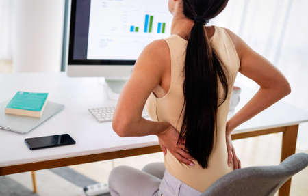 Overworked woman with back pain in office with bad postureの写真素材