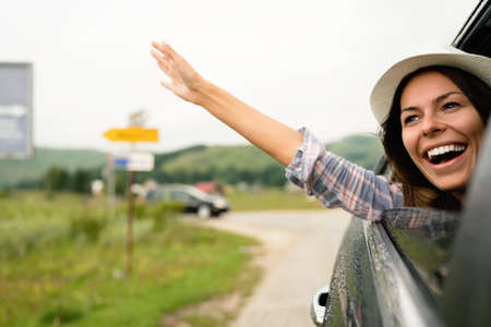Woman in car road trip waving out the window smiling