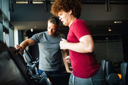 Fat young men with trainer exercising at fitness gym.