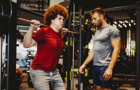Overweight young man exercising gym with personal trainer