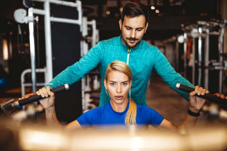 Happy fit woman exercising with her personal trainer in gymの写真素材