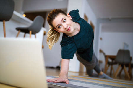 Smiling woman exercising at home and watching training videos on laptop.