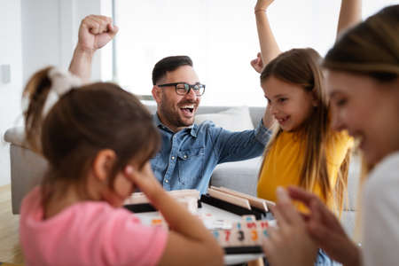 Happy young parents and children having fun, playing board game at homeの写真素材