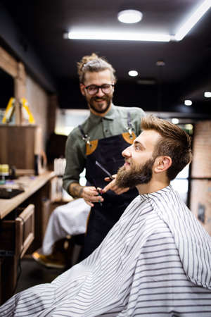 Portrait of happy young barber with client at barbershop and smiling.の写真素材