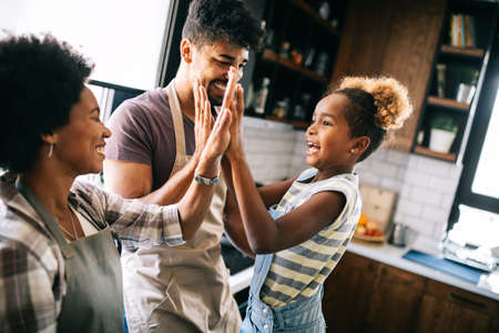 Happy girl and her beautiful parents are smiling while cooking in kitchen at homeの写真素材