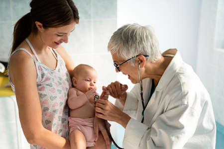Pediatrician doctor medical examining little smiling baby, held by motherの写真素材