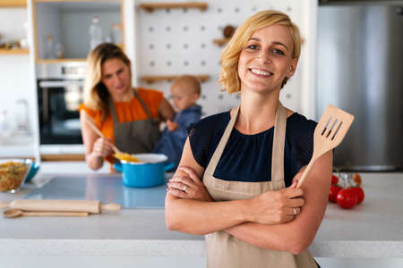 Happy lesbian couple with child preparing food at home togetherの写真素材