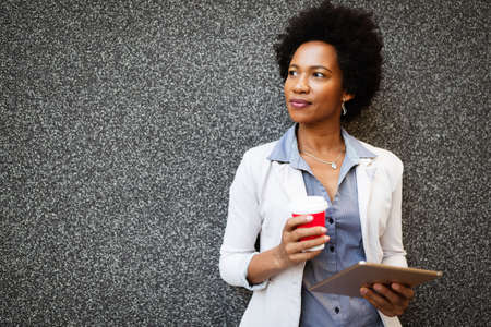 Portrait of smiling african woman walking in the city with tabletの写真素材