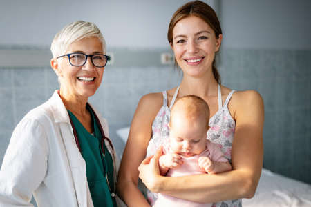 Mother holding adorable baby with smiling pediatrician doctor in hospitalの写真素材