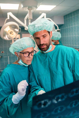 Team of surgeon doctors looking at x-ray film before surgery to set up diagnosisの写真素材