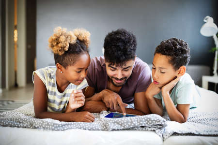 Happy father and children having fun with tablet, smiling at funny video, playing gameの写真素材