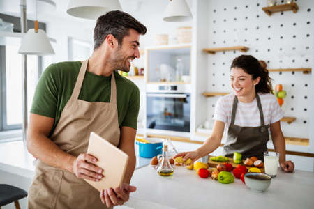 Happy young couple preparing food in kitchen at homeの写真素材