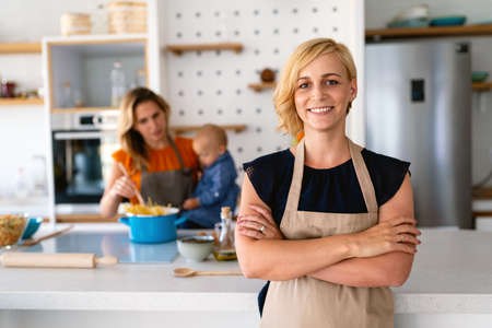 Smiling young woman chef cook in apron standing at the kitchenの写真素材