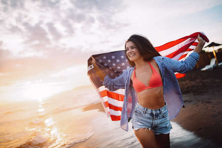 Cheerful happy woman outdoors on the beach holding USA flag having fun.