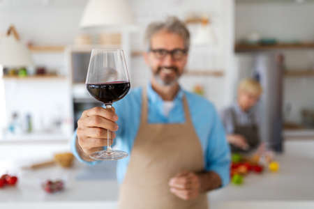 Happy senior couple cooking together and drinking wine in home kitchenの写真素材