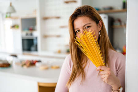 Portrait of beautiful woman with pasta at her kitchen, preparing to cookの写真素材