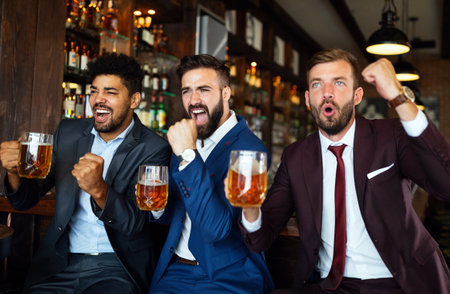 Men fans screaming and watching football on TV and drink beer in a pubの写真素材