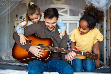Smiling father with multiethnic children having fun and playing guitar at homeの写真素材