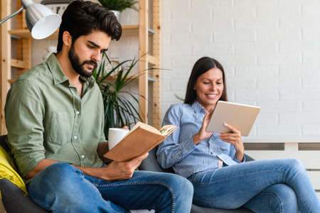 Free time together. Happy couple is spending weekend together at home. Reading book, tablet.