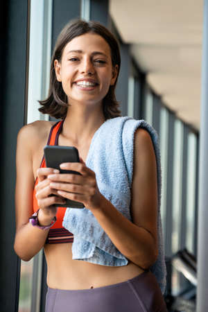 Portrait of a cheerful woman using smartphone in fitness gymの写真素材