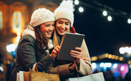 Happy women friends using digital tablet for online shopping at Christmas in the city.の写真素材