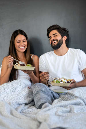 Healthy breakfast in bed. Young beautiful couple in love is sitting on bed and having breakfast.の写真素材