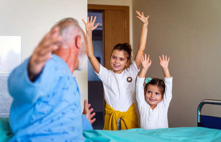 Happy grandchildren visiting grandfather at hospital ward. Support, family and healthcare concept.の写真素材