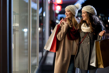 Two beautiful happy women with shopping bags in the city next to shop window backgroundの写真素材