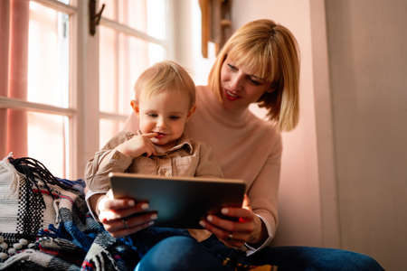 Happy family technology concept. Smiling mother and her toddler son playing with digital tablet