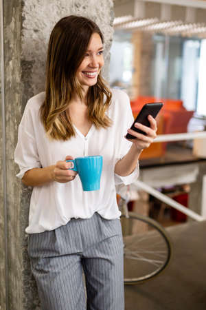 Portrait of a happy young success woman using smartphone and drinking coffee in breakの写真素材