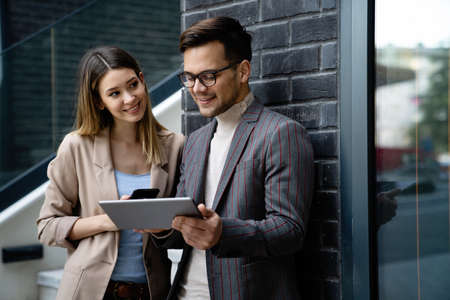 Businessman and businesswoman discussing working together in urban background outdoors.