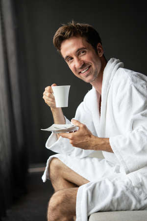 Young handsome man drinking morning coffee in bathrobeの写真素材