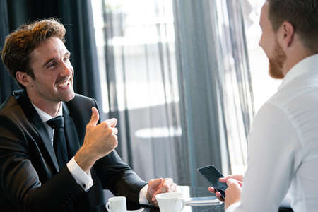 Image of young businessman with cup of coffee communicating with colleague
