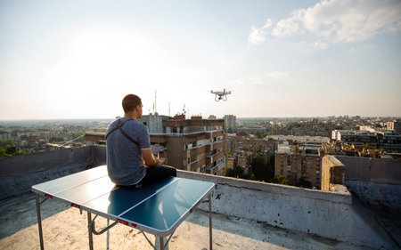 Young technician flying UAV drone with remote control on rooftop