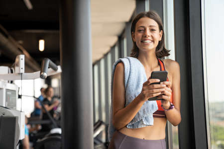Portrait of a cheerful sports woman using smartphone in fitness gymの写真素材