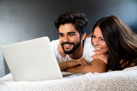 Couple with laptop in bed reading news and smilingの写真素材