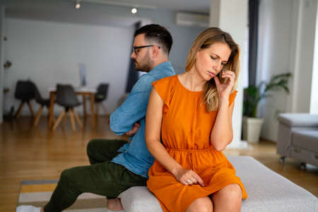 Sad pensive couple thinking of relationships problems sitting on sofa, conflicts in marriage.