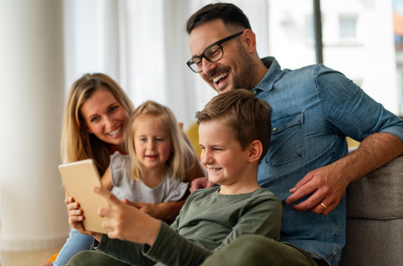 Happy young family having fun time at home. Parents with children using digital device.