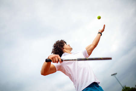 Young handsome tennis player with racket and ball prepares to serve at beginning of game or match.