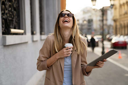 Attractive businesswoman drinking a coffee and using a digital tablet while enjoying breakの写真素材